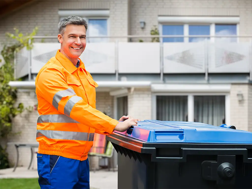 Smiling Man in Orange Vest Pushing a Trash Can
